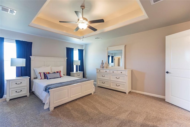 bedroom featuring ceiling fan, light colored carpet, a tray ceiling, and multiple windows