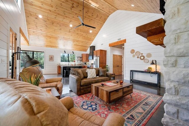 living room with a stone fireplace, high vaulted ceiling, wooden walls, wood ceiling, and dark wood-type flooring