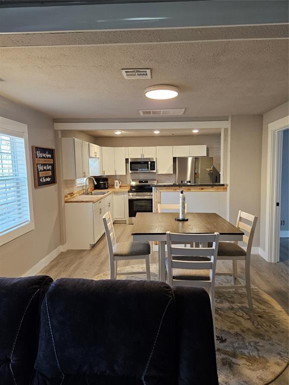 dining room with sink, a textured ceiling, and light hardwood / wood-style floors