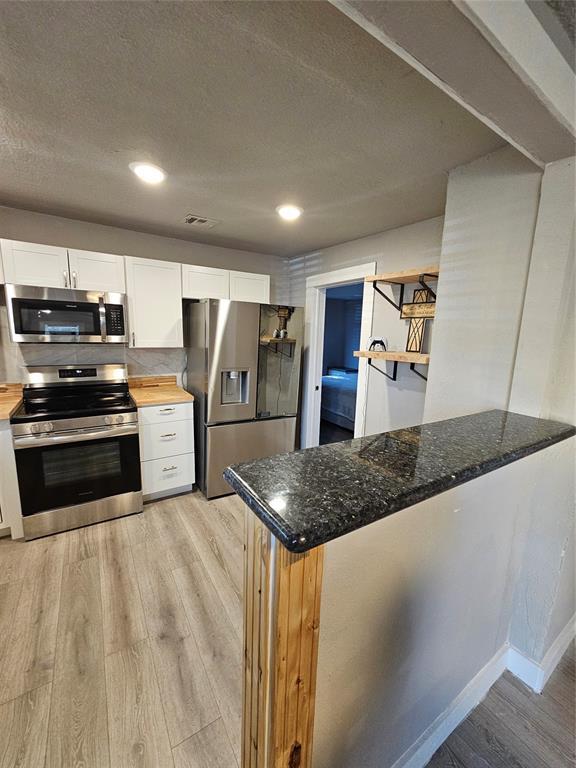 kitchen with white cabinetry, wood counters, stainless steel appliances, and light hardwood / wood-style flooring