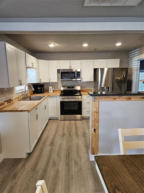 kitchen with appliances with stainless steel finishes, white cabinetry, sink, wooden counters, and light hardwood / wood-style floors