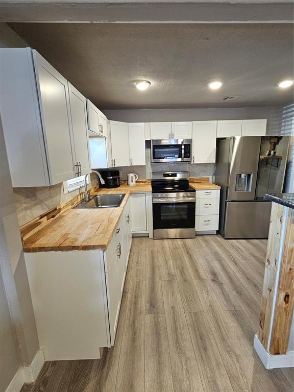 kitchen featuring butcher block counters, sink, appliances with stainless steel finishes, light hardwood / wood-style floors, and white cabinets