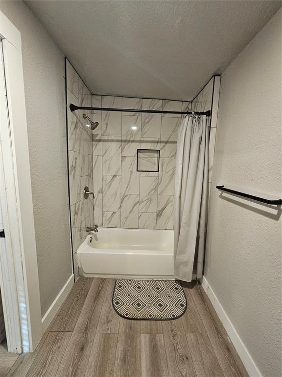 bathroom with a textured ceiling, wood-type flooring, and shower / bath combo