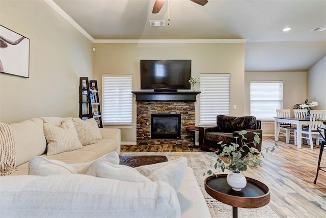 living room with crown molding, wood-type flooring, a stone fireplace, and ceiling fan