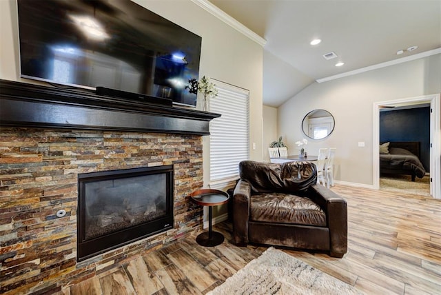 living room featuring crown molding, vaulted ceiling, light hardwood / wood-style floors, and a stone fireplace