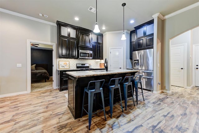 kitchen featuring sink, light stone counters, a center island with sink, appliances with stainless steel finishes, and pendant lighting