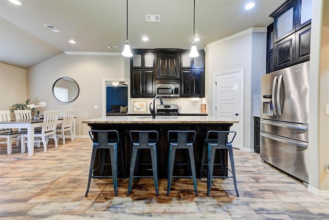 kitchen featuring light stone counters, tasteful backsplash, hanging light fixtures, a center island with sink, and stainless steel appliances