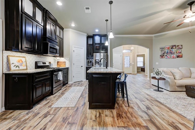 kitchen featuring a kitchen bar, hanging light fixtures, appliances with stainless steel finishes, an island with sink, and light stone countertops