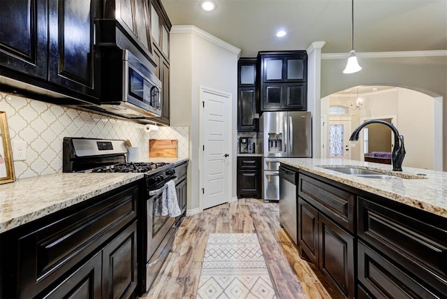 kitchen featuring sink, hanging light fixtures, appliances with stainless steel finishes, light stone countertops, and light hardwood / wood-style floors