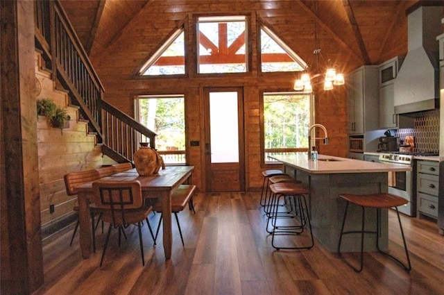 kitchen with gray cabinets, wood walls, sink, stainless steel gas range, and wall chimney exhaust hood