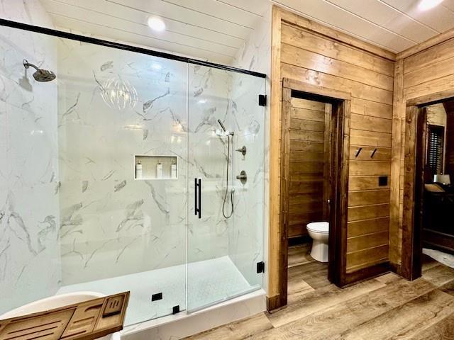 bathroom with an enclosed shower, wood-type flooring, toilet, and wood walls