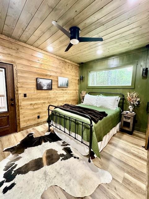 bedroom featuring ceiling fan, light hardwood / wood-style floors, wooden ceiling, and wood walls