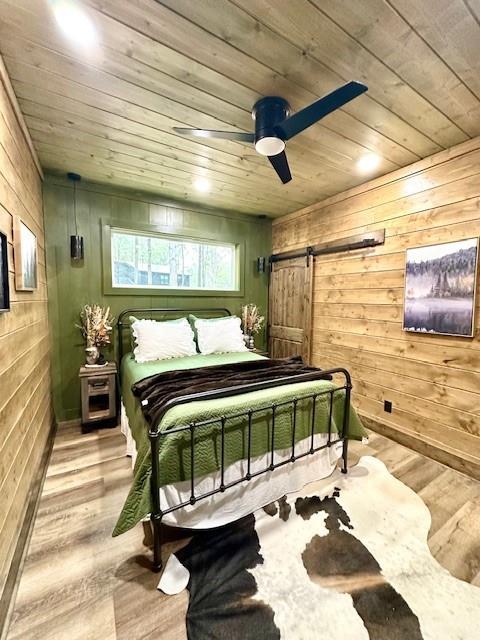 bedroom featuring light hardwood / wood-style floors, a barn door, wooden ceiling, and wood walls