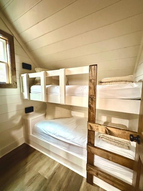 unfurnished bedroom with lofted ceiling, wood ceiling, wood-type flooring, and wooden walls