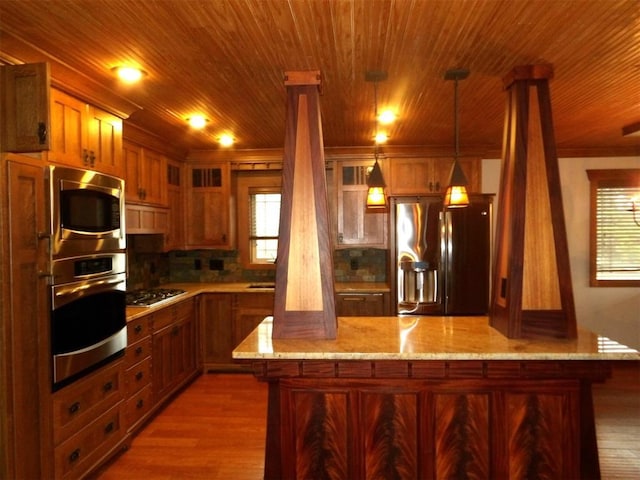 kitchen with light stone countertops, appliances with stainless steel finishes, wood-type flooring, and pendant lighting