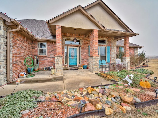 doorway to property featuring a shingled roof, a patio, stone siding, stucco siding, and brick siding