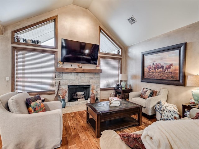 living room featuring lofted ceiling, a stone fireplace, and light wood-type flooring