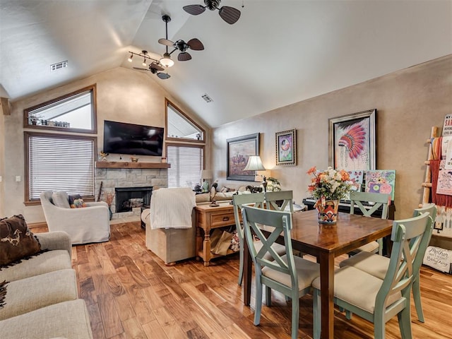 dining space featuring ceiling fan, light wood-style flooring, a fireplace, visible vents, and vaulted ceiling