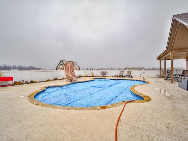 view of swimming pool with a fenced backyard, a water slide, and a patio