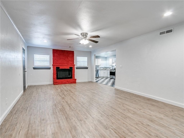 unfurnished living room featuring sink, ornamental molding, ceiling fan, a brick fireplace, and light wood-type flooring