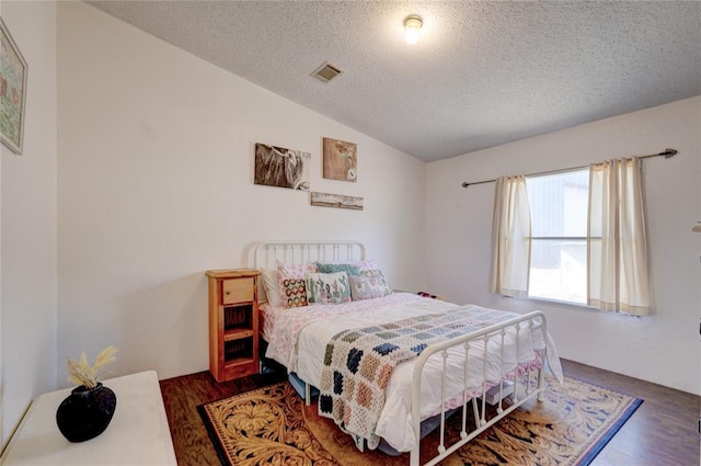 bedroom with dark wood-type flooring, vaulted ceiling, and a textured ceiling