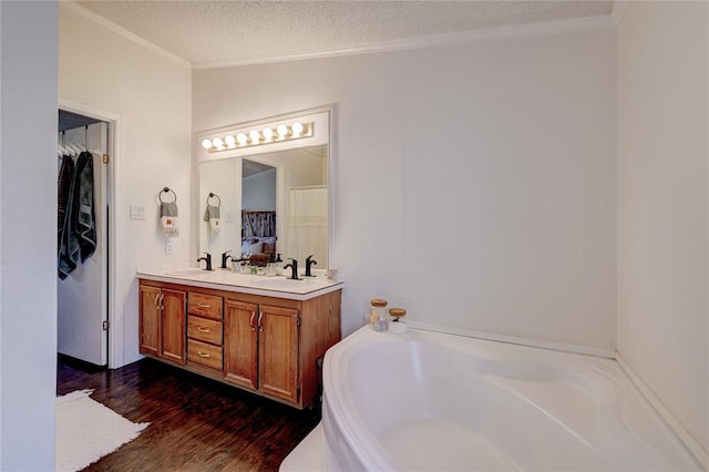 bathroom with hardwood / wood-style flooring, a bathtub, vanity, ornamental molding, and a textured ceiling