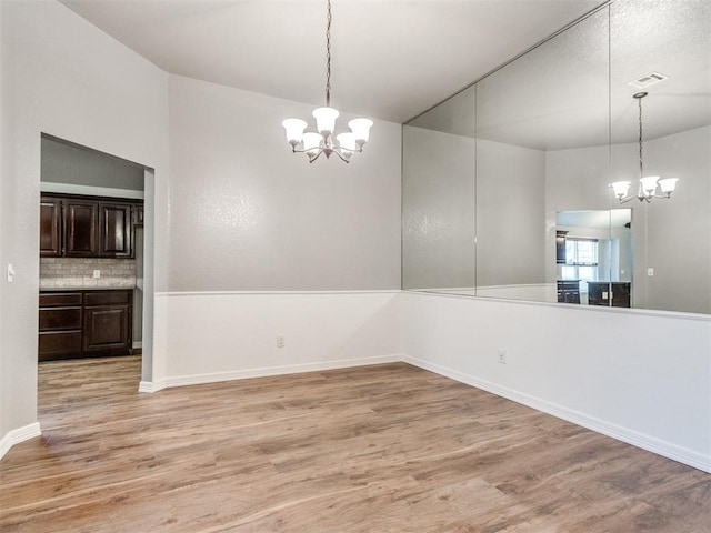 unfurnished dining area featuring an inviting chandelier and light hardwood / wood-style flooring