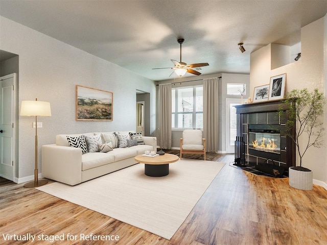 living room with a tile fireplace, wood-type flooring, and ceiling fan