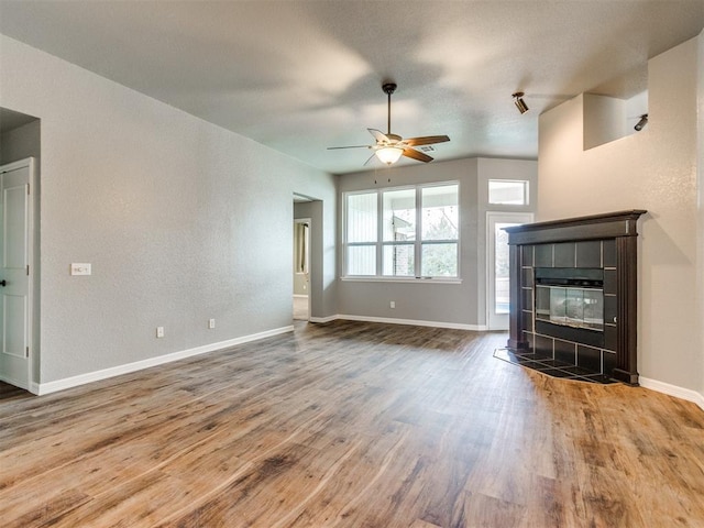 unfurnished living room with a tile fireplace, wood-type flooring, and ceiling fan