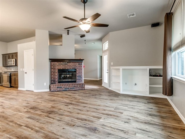 unfurnished living room with ceiling fan, a brick fireplace, and light hardwood / wood-style flooring