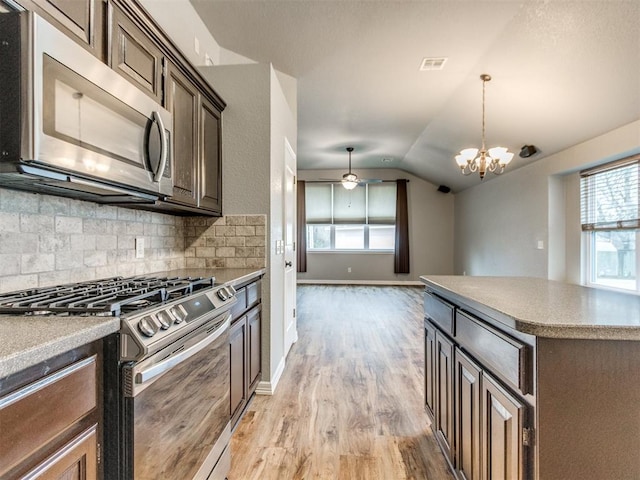 kitchen with lofted ceiling, tasteful backsplash, decorative light fixtures, dark brown cabinets, and appliances with stainless steel finishes