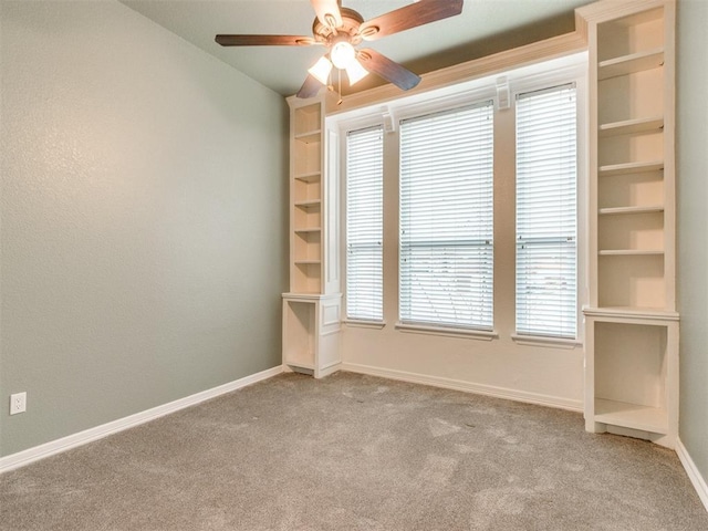 spare room featuring light carpet, built in features, and ceiling fan