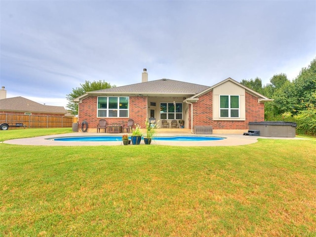 rear view of property featuring a swimming pool with hot tub, a patio area, and a lawn