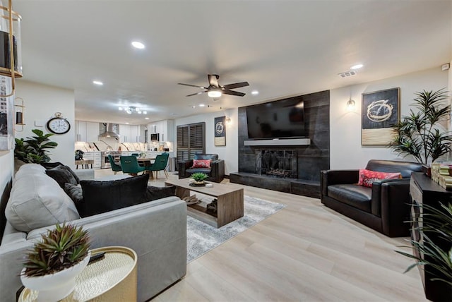 living room featuring ceiling fan, a fireplace, and light hardwood / wood-style flooring