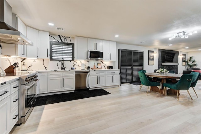 kitchen with white cabinetry, appliances with stainless steel finishes, light hardwood / wood-style floors, and wall chimney range hood