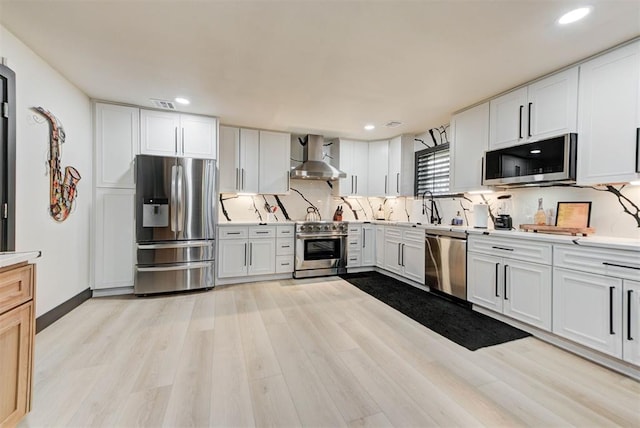 kitchen with wall chimney exhaust hood, white cabinetry, appliances with stainless steel finishes, and decorative backsplash