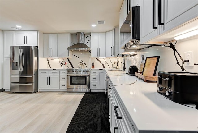 kitchen with wall chimney exhaust hood, appliances with stainless steel finishes, sink, and white cabinets