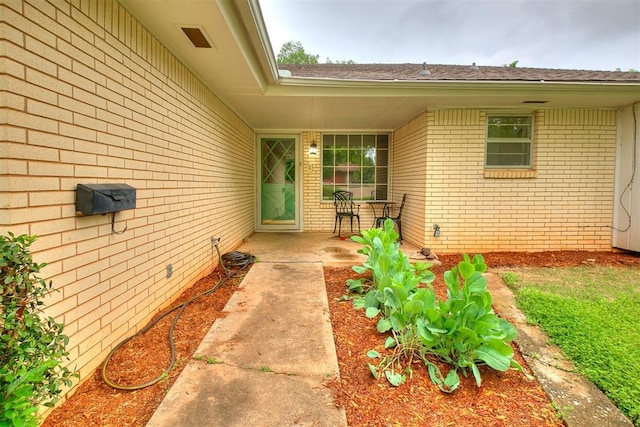 doorway to property featuring roof with shingles, a patio, and brick siding