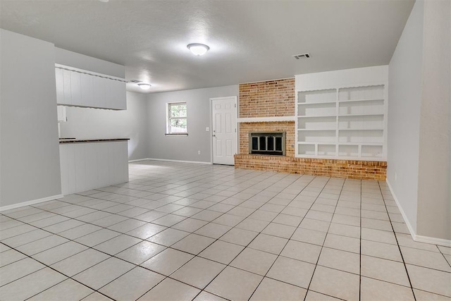 unfurnished living room with a brick fireplace, built in shelves, baseboards, light tile patterned floors, and visible vents