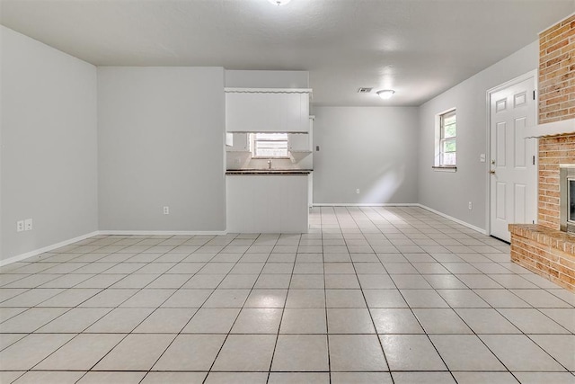 unfurnished room with light tile patterned floors, baseboards, a fireplace, and visible vents