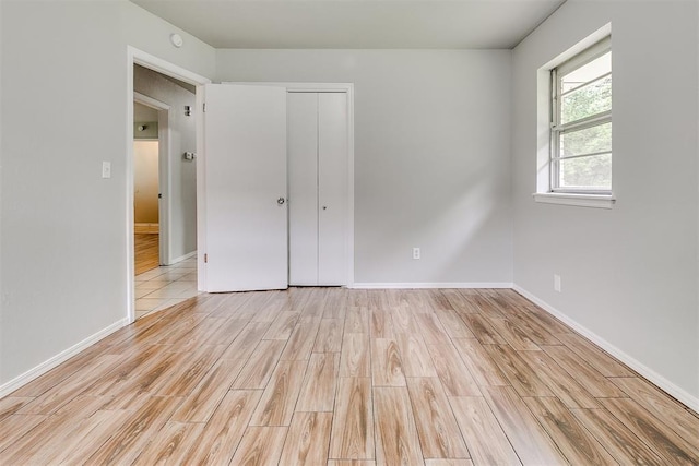 unfurnished bedroom with light wood-type flooring, baseboards, and a closet