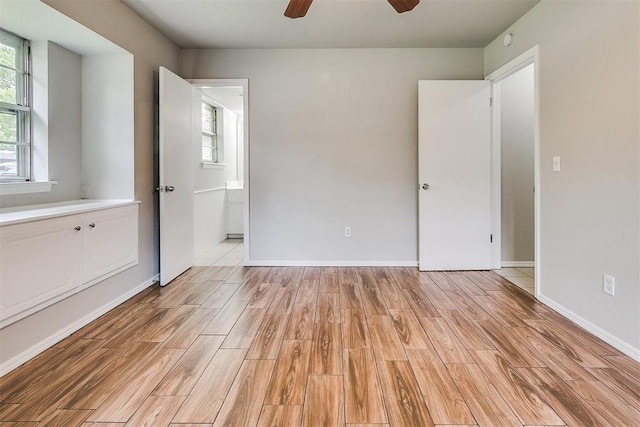unfurnished bedroom with baseboards, a ceiling fan, light wood finished floors, and ensuite bath