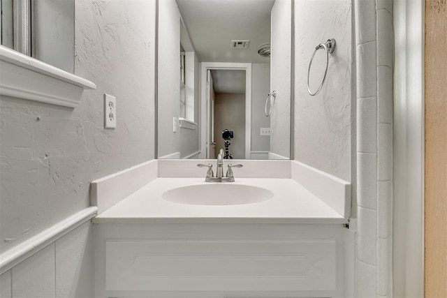 bathroom featuring visible vents, a textured wall, and vanity