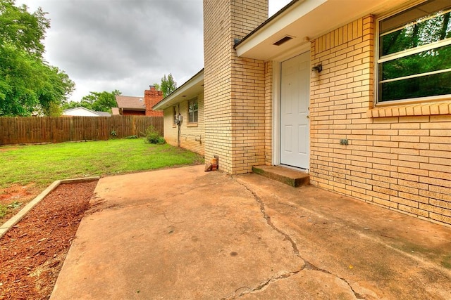 entrance to property with fence, a patio, a chimney, brick siding, and a yard