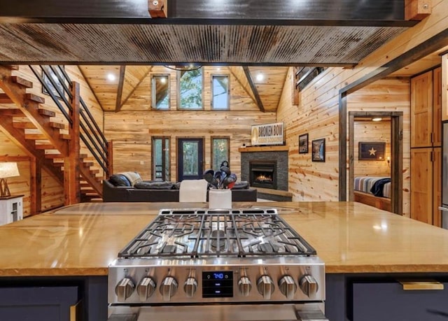 kitchen featuring a stone fireplace, wooden walls, lofted ceiling with beams, and stainless steel range oven