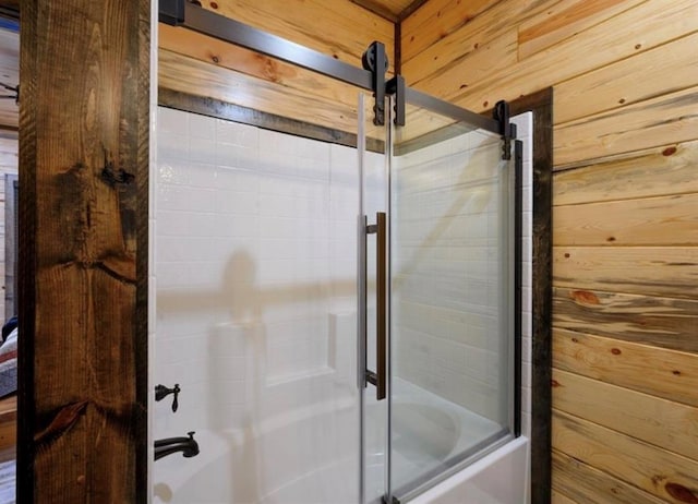 bathroom featuring wooden walls and shower / bath combination with glass door