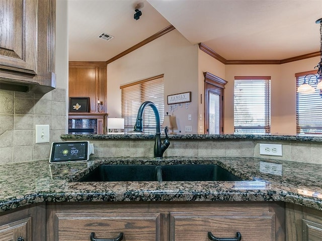 kitchen with ornamental molding, dark stone countertops, sink, and pendant lighting