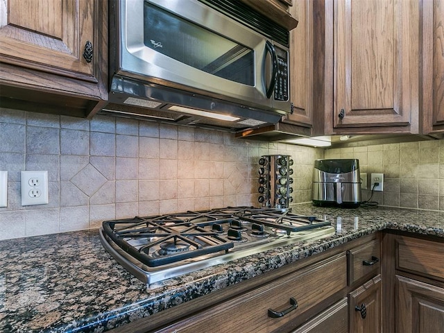 kitchen featuring dark stone countertops, decorative backsplash, stainless steel appliances, and dark brown cabinetry