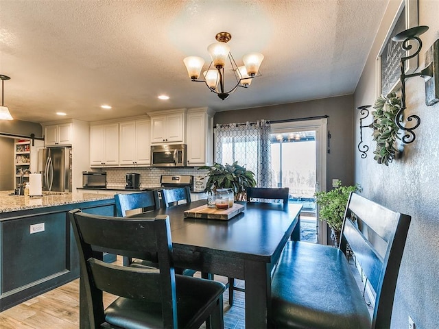 dining area featuring sink, an inviting chandelier, a textured ceiling, a barn door, and light wood-type flooring