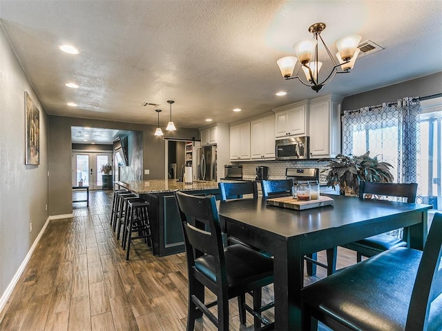 dining space featuring french doors, dark hardwood / wood-style flooring, a textured ceiling, and a notable chandelier